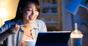 (woman enjoying ramen at her computer)
