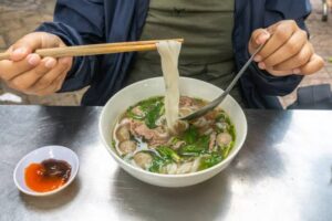 (eating an instant pho bowl) Female hand using chopsticks and spoon while having pho noodle soup